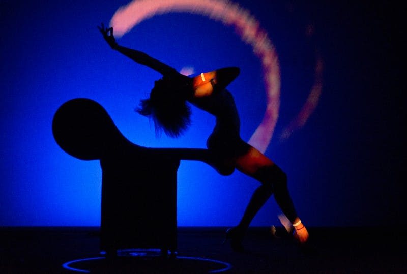 의자가 있는 선명한 파란색과 자홍색 배경에 실루엣으로 표현력 있는 댄스 포즈를 취하는 사람.