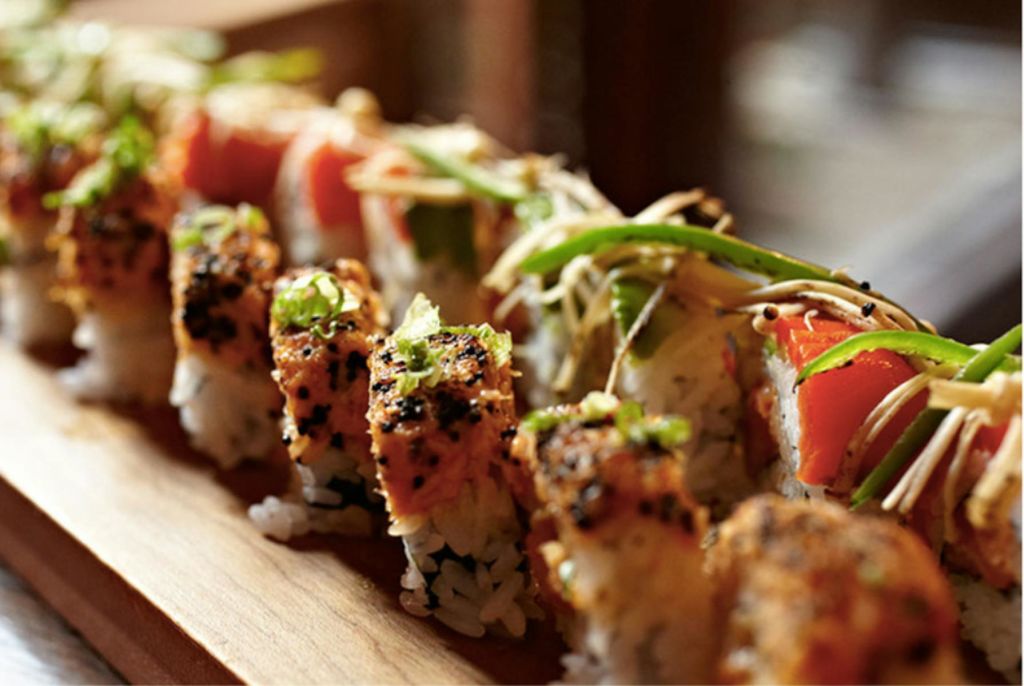 나무 서빙 보드에 파와 참깨로 장식된 초밥 롤의 클로즈업.