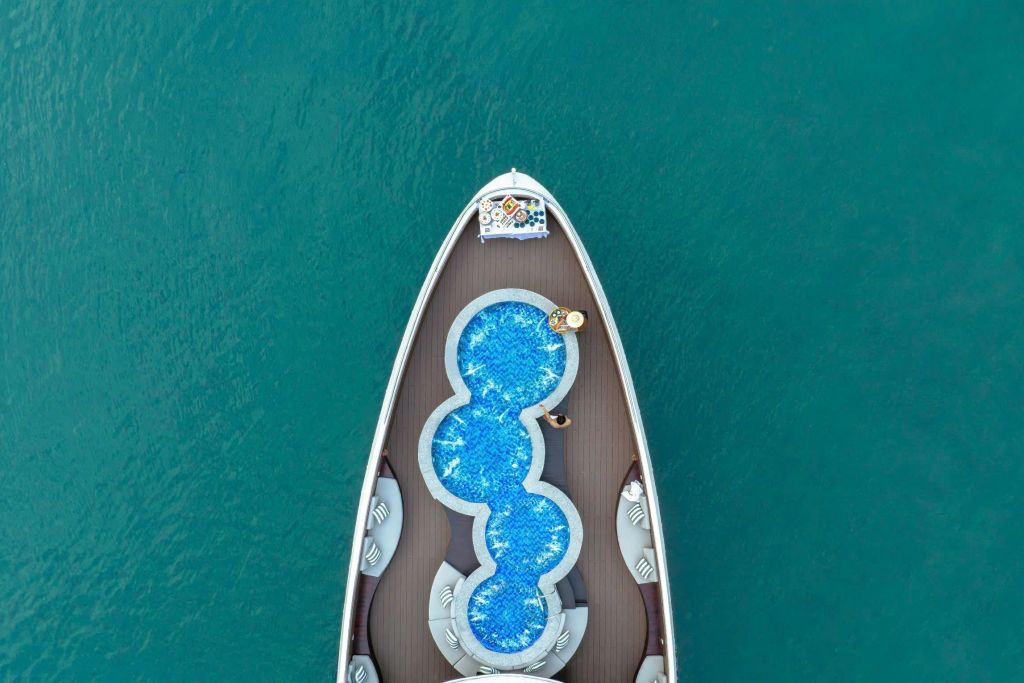 독특한 다구간 수영장과 맑고 푸른 바다에서 휴식을 취하는 두 사람이 있는 요트 활의 공중 전망.