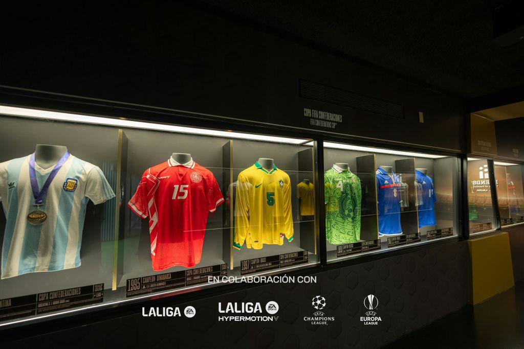 유리 패널이 있는 어두운 방 내부에 각기 숫자로 표시된 다양한 축구 유니폼을 보여주는 디스플레이 케이스.