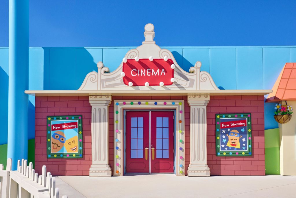 빨간색 간판, 장식 기둥, 빨간색 이중 문 양쪽에 "Now Showing" 포스터가 있는 다채로운 영화관 입구.