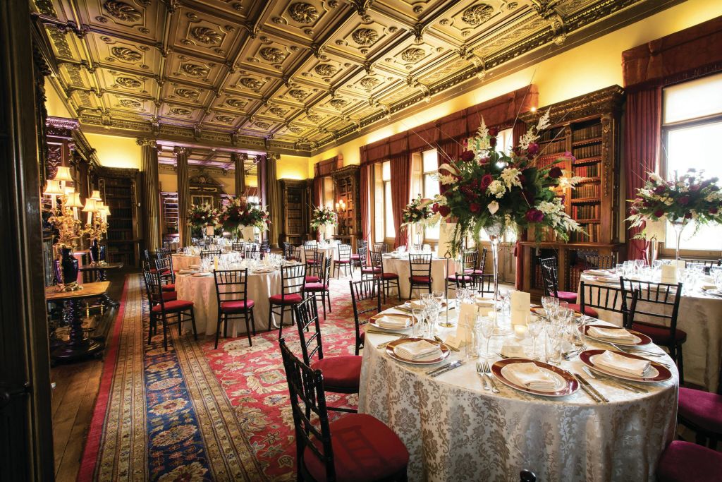 이벤트를 위한 원형 테이블, 정교한 천장, 대형 꽃무늬 센터피스, 책장, 무늬 카펫이 있는 우아한 다이닝 룸.