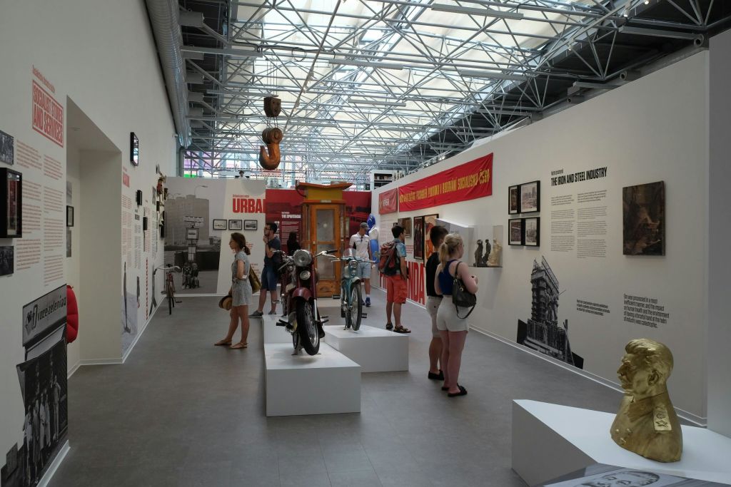 빈티지 오토바이, 정보 디스플레이, 산업 테마 장식이 있는 도시 테마 박물관을 탐험하는 사람들.