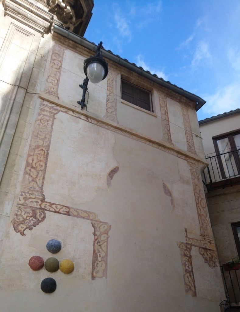 높은 베이지색 건물에 장식 장식, 가로등, 색색의 공이 벽에 설치되어 있습니다. 하늘이 부분적으로 보인다.