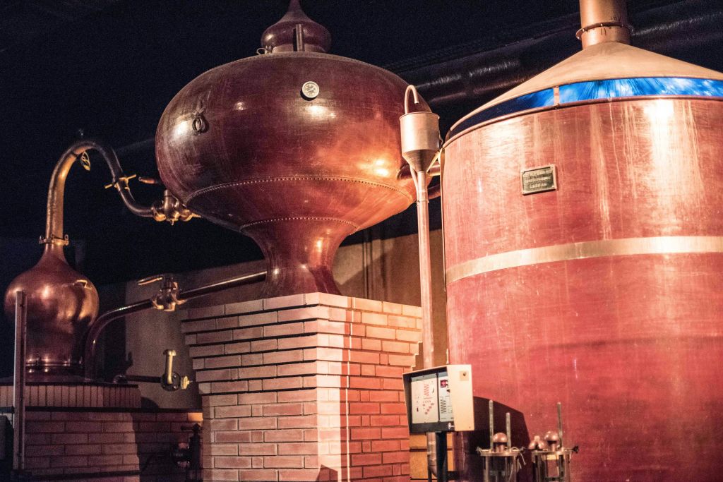 증류소 내부에 벽돌 베이스가 있는 대형 구리 증류 탱크에는 파이프와 제어판이 있습니다.