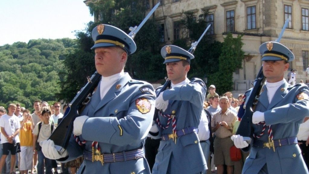 밝은 파란색 유니폼을 입은 병사들이 역사적인 건물 앞에서 군중을 지나가고 있습니다.