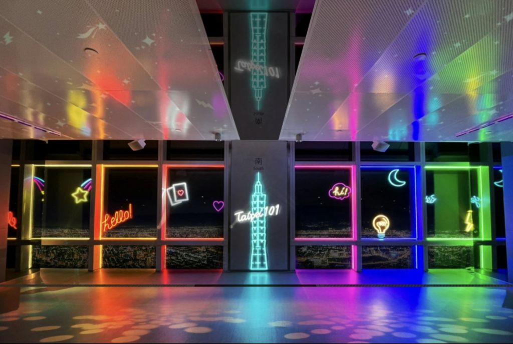 "Hello!", "Taipei 101" 등 네온사인이 있는 밝은 복도와 커다란 창문을 통해 바라보는 도시 풍경.