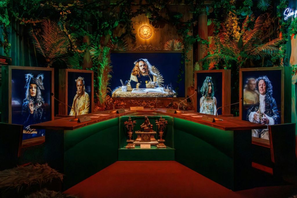 초록색 책상, 역사적 인물의 액자 초상화, 무성한 녹지를 배경으로 한 객실입니다.