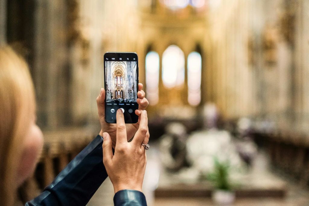 스마트폰을 들고 높은 아치와 스테인드글라스 창문이 있는 화려한 교회 내부의 이미지를 캡처한 사람.