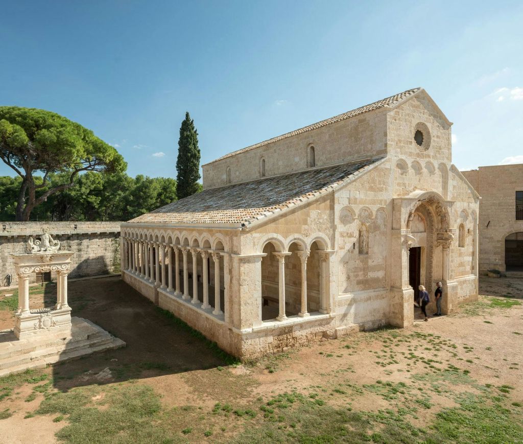 화창한 날 입구 근처에 아치형 콜로네이드, 타일 지붕, 두 사람이 있는 중세 석조 교회.
