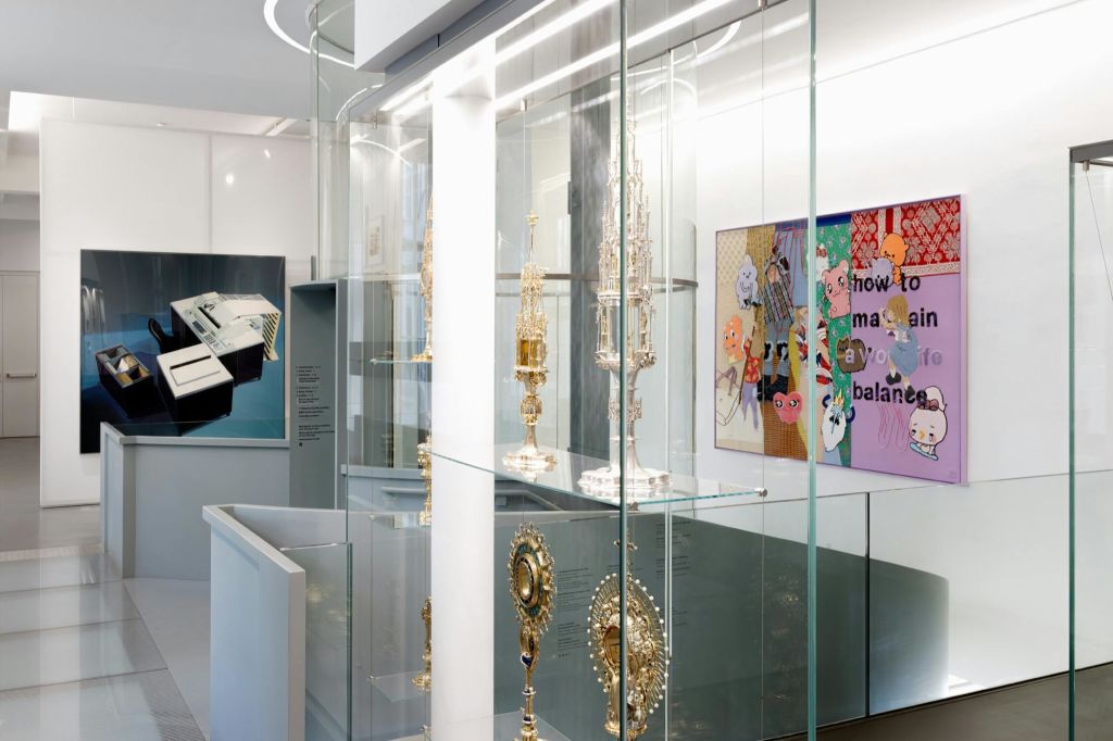 현대적인 박물관 환경에서 화려한 금속 유물이 담긴 유리 디스플레이 케이스, 벽에 걸린 예술품.