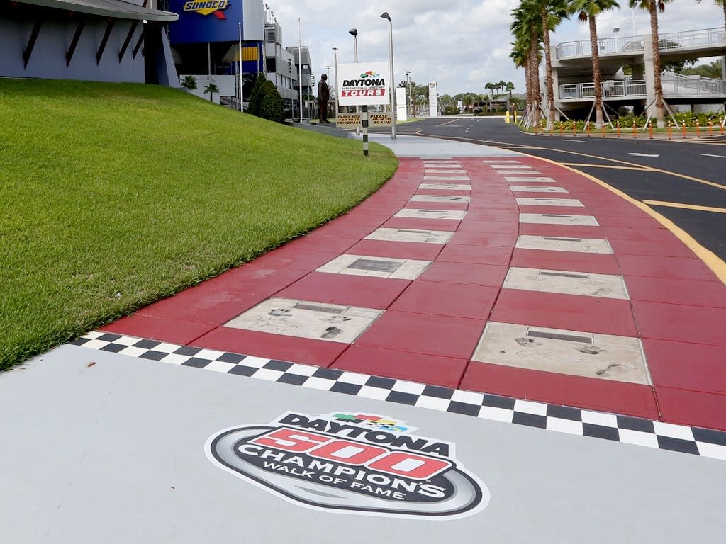 모터스포츠 경기장에서 "Daytona 500 Champions Walk of Fame" 이라는 라벨이 붙은 핸드프린트와 시그니처가 있는 빨간색과 흰색 체크무늬 산책로.