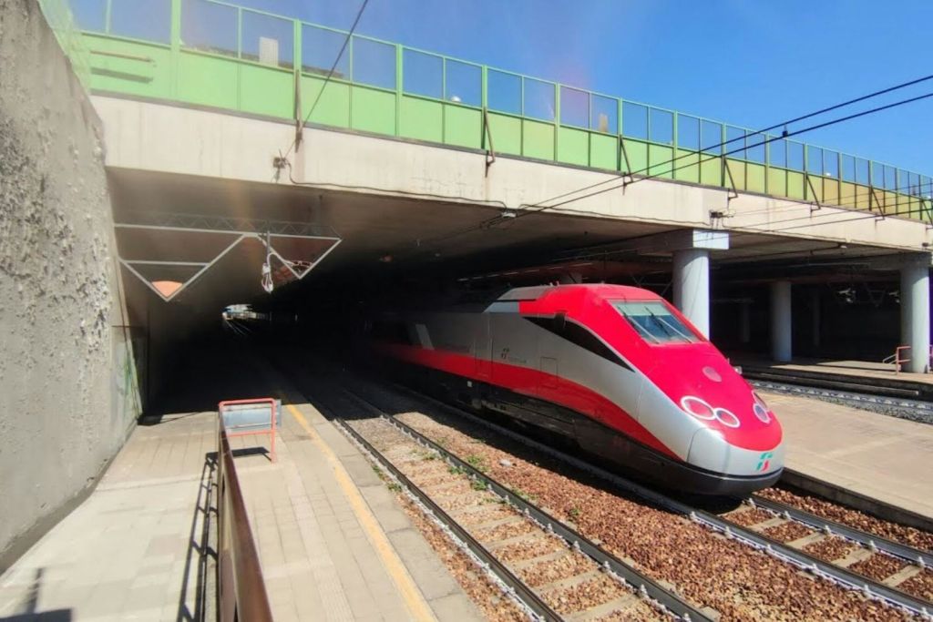 화창한 날 초록색 다리 아래 터널에서 빨간색과 흰색의 고속 열차가 등장합니다.