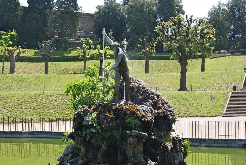 녹음으로 둘러싸인 바위 분수의 석상. 배경에는 나무와 다듬어진 잔디밭이 보입니다.