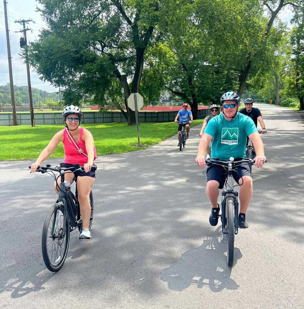 화창한 날 나무와 잔디로 둘러싸인 포장 도로에서 자전거를 타는 사람들의 모임.