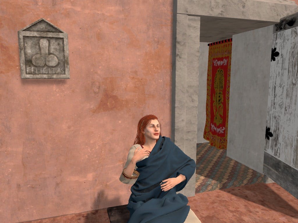 파란색 천을 두른 긴 빨간색 머리카락을 가진 사람이 출입구 근처에 화려한 커튼이 있는 질감의 벽에 앉아 있습니다.