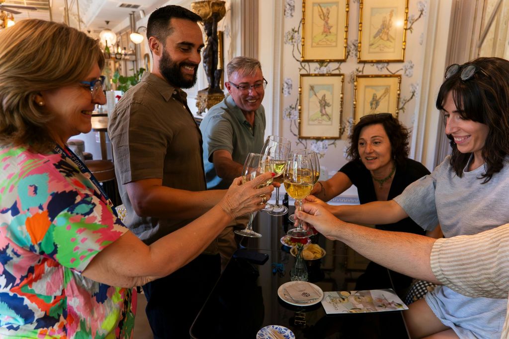 간식과 함께 식탁에 둘러앉은 토스트에서 다섯 명이 잔을 들어 올립니다. 액자에 담긴 예술 작품과 화려한 인테리어가 돋보이는 공간입니다.