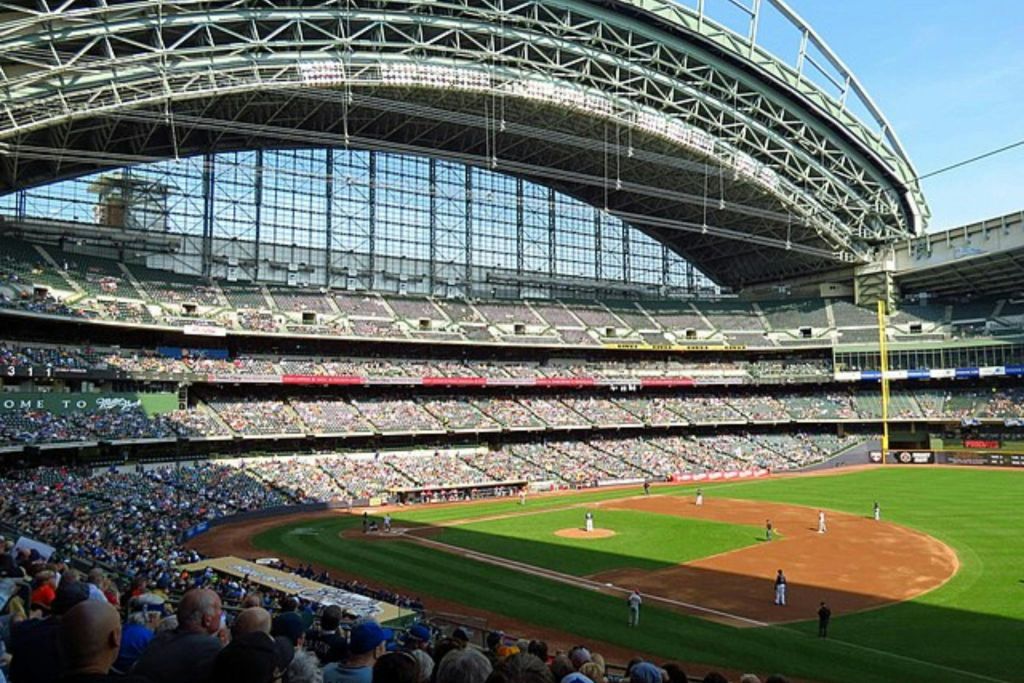 지붕이 부분적으로 닫혀 있고 스탠드에는 많은 관중이 있는 대형 경기장에서 진행 중인 야구 경기.