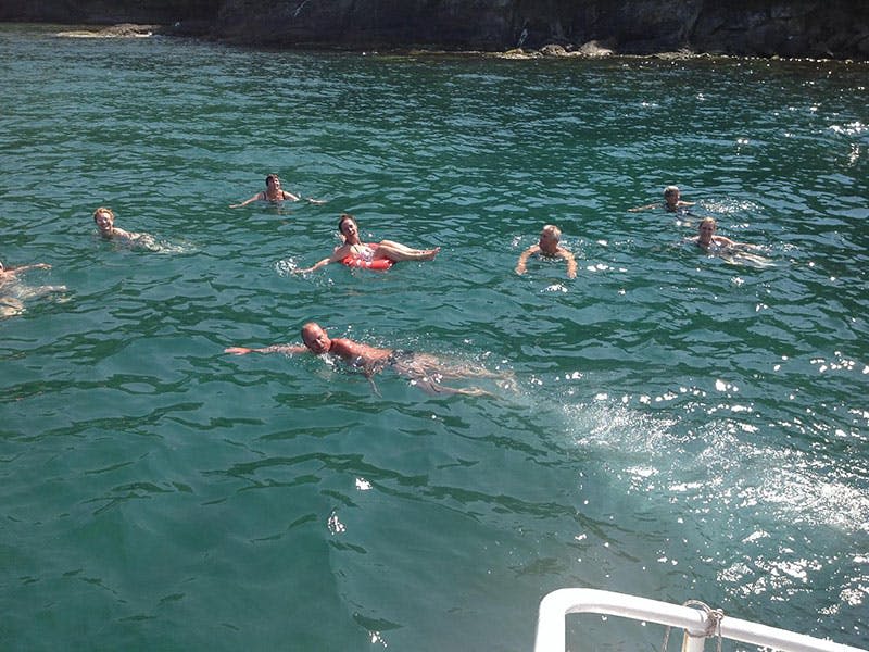 바위가 많은 해안가 근처의 맑고 푸른 물에 여러 사람이 헤엄치고 떠 있습니다.