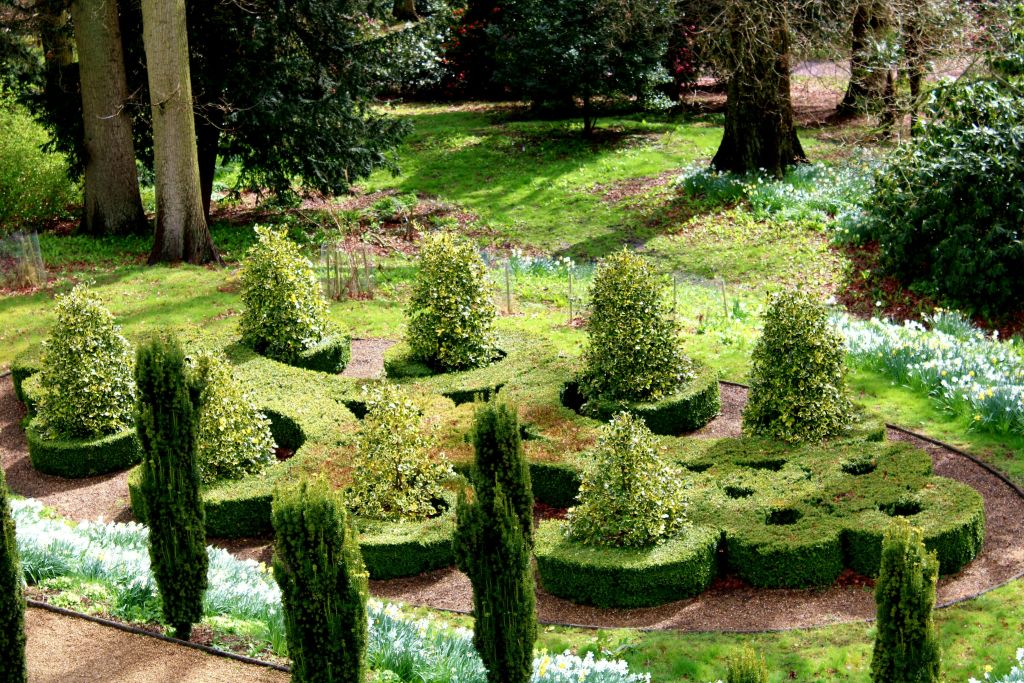 정교한 모양의 울타리, 작은 수풀, 커다란 나무를 배경으로 주변의 잔디가 우거진 정원이 잘 정비되어 있습니다.