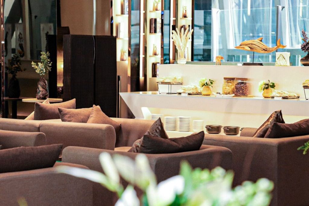 갈색 소파, 간식과 항아리를 전시한 카운터, 책과 인테리어 소품이 놓인 장식 선반이 있는 현대적인 라운지 공간입니다.