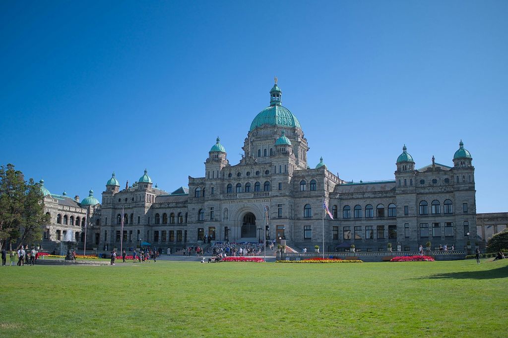 녹색 돔과 대칭형 외관이 있는 크고 유서 깊은 건물입니다. 계단에 사람들이 모여 있고, 앞쪽에는 초록색 잔디밭이 있습니다.