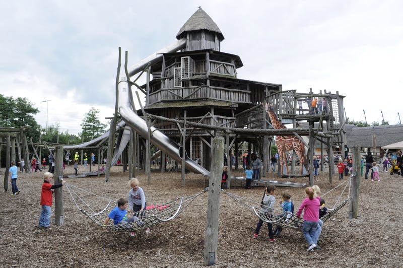 미끄럼틀과 기린 조형물이 있는 커다란 나무 놀이터 구조물 앞에서 아이들이 밧줄 그네를 타고 놀고 있습니다.