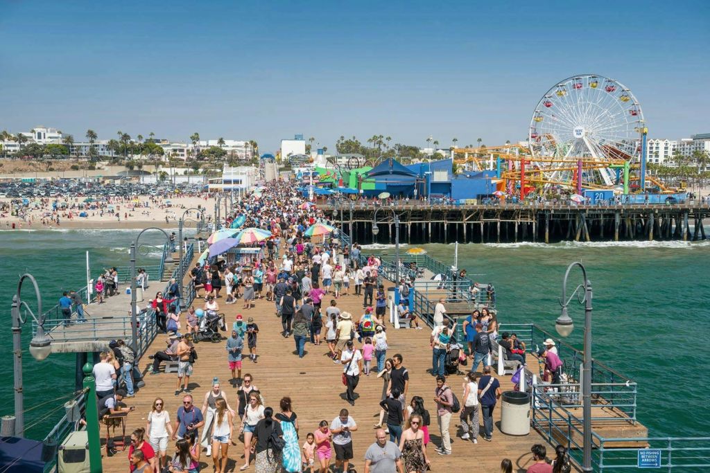해변, 다채로운 색상의 건축물, 대관람차를 배경으로 북적거리는 부두를 거닐고 있는 사람들로 북적거립니다.