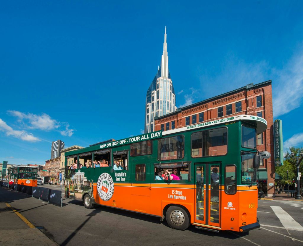 탑승객이 탑승하는 2층 투어 버스와 "Hop on Hop off" 표지판이 높은 현대적인 건물 앞에 주차되어 있습니다.