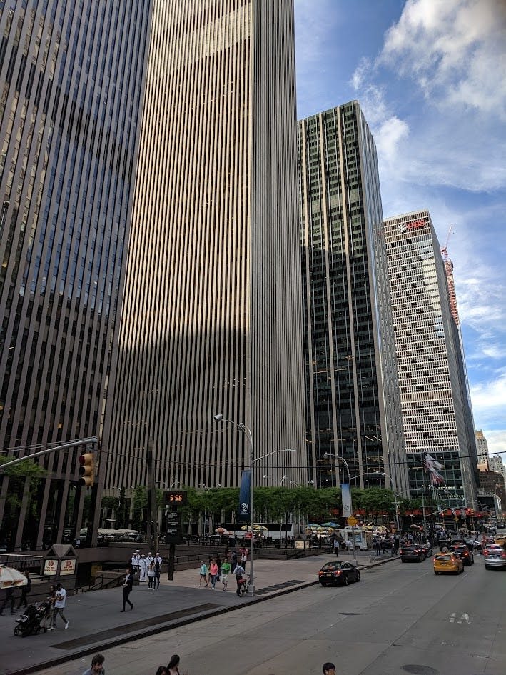 부분적으로 흐린 하늘 아래 높은 사무실 건물, 보행자, 자동차, 택시가 있는 도시 거리.