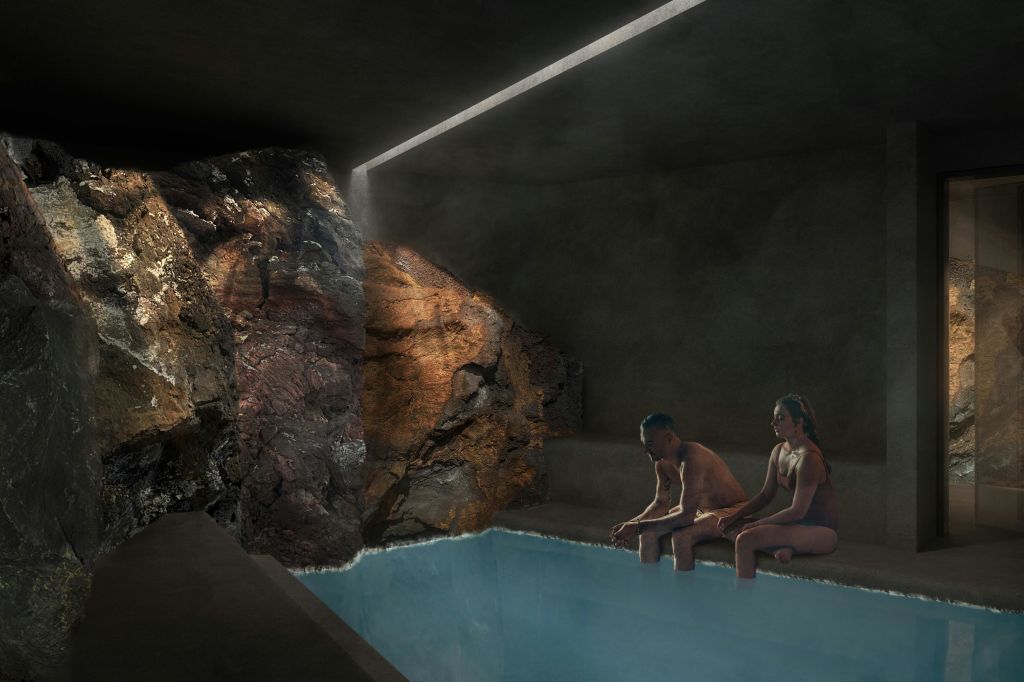 자연 암벽과 현대적인 미니멀리즘 디자인이 돋보이는 작은 실내 수영장 근처에 두 사람이 앉아 있습니다.