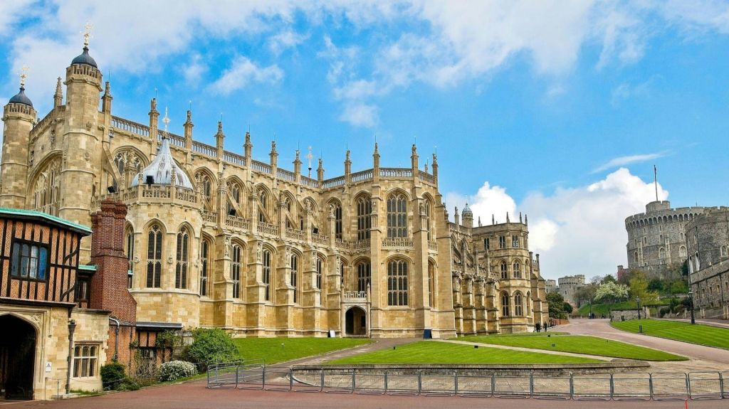 화려한 첨탑과 커다란 창문이 있는 고딕 양식의 건물로, 구름이 낀 푸른 하늘 아래 푸른 잔디밭으로 둘러싸여 있습니다.