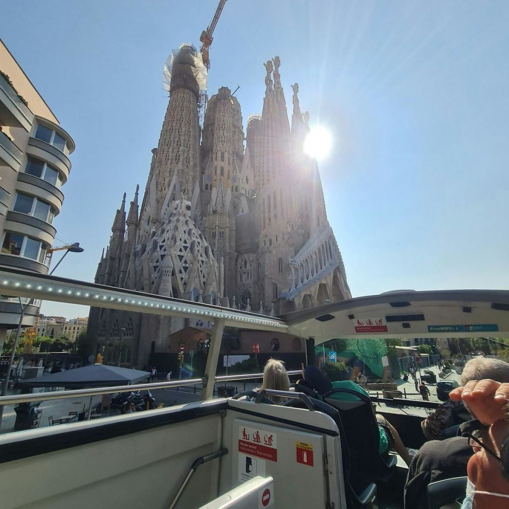 사그라다 파밀리아 (Sagrada Família) 를 내려다보는 오픈탑 버스를 탄 관광객들은 대성당 위에 건설 크레인을 설치하고 맑은 하늘을 감상할 수 있습니다.