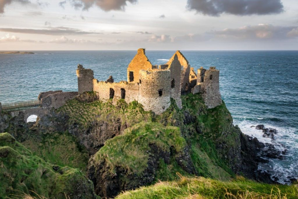 흐린 하늘 아래 바다가 내려다보이는 잔디 절벽 꼭대기에 자리한 유서 깊은 석조 성터.