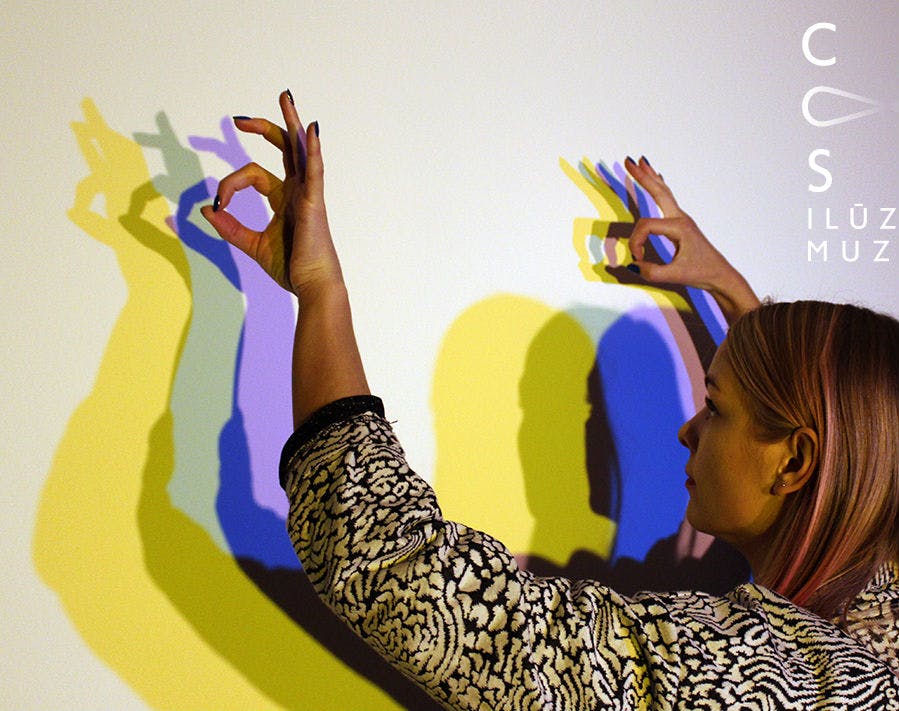 노란색, 파란색 및 보라색 빛 투영이 겹쳐진 흰색 벽에 화려한 손 그림자를 만드는 사람.