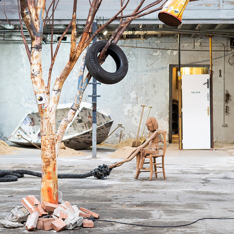 페인트 나무에 타이어 그네, 의자에 나무 피규어, 흩어져 있는 벽돌, '살리다' 라고 적힌 열린 문이 있는 버려진 공방.