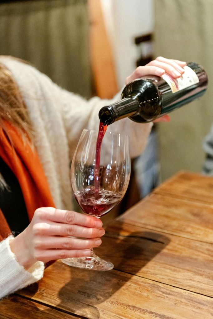 나무 테이블 위에 놓인 와인잔에 레드 와인을 붓는 사람.