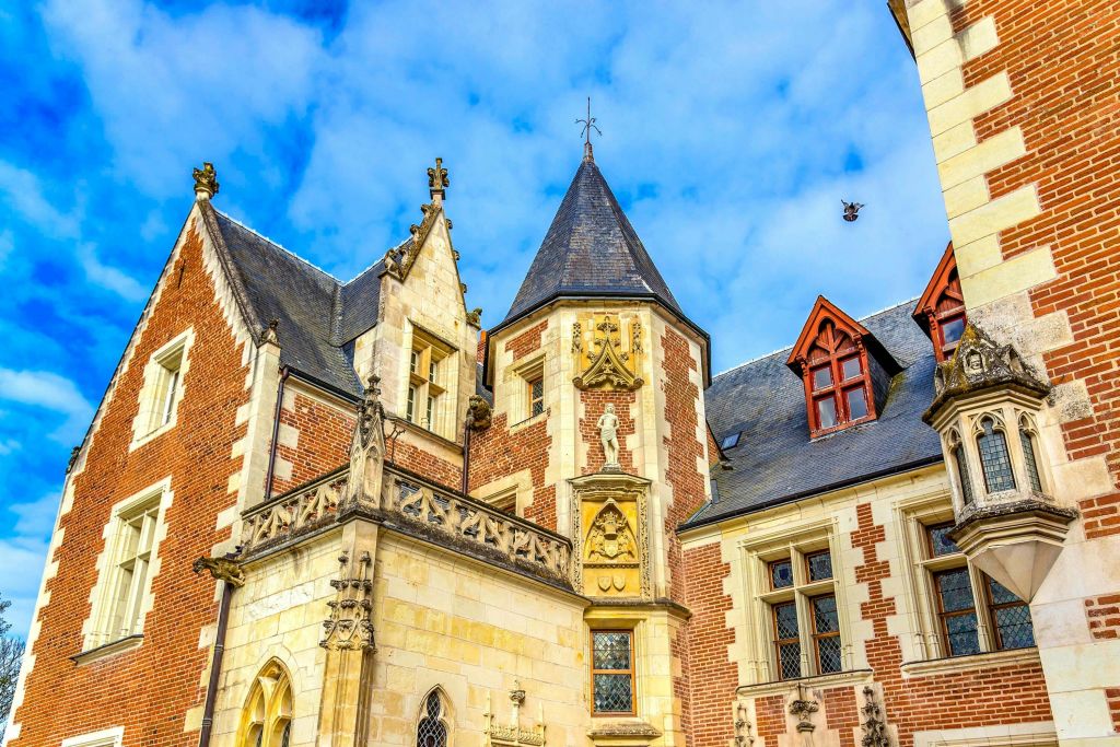 정교한 건축 디테일, 높은 뾰족한 지붕, 푸른 하늘을 배경으로 한 유서 깊은 벽돌과 석조 건물.