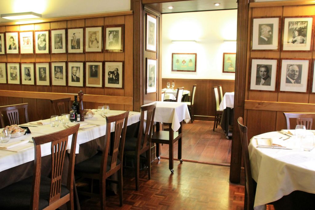 흰색 식탁보, 나무 의자, 나무 패널 벽에 액자 사진, 부드러운 조명 식탁 공간이 있는 아늑한 레스토랑입니다.