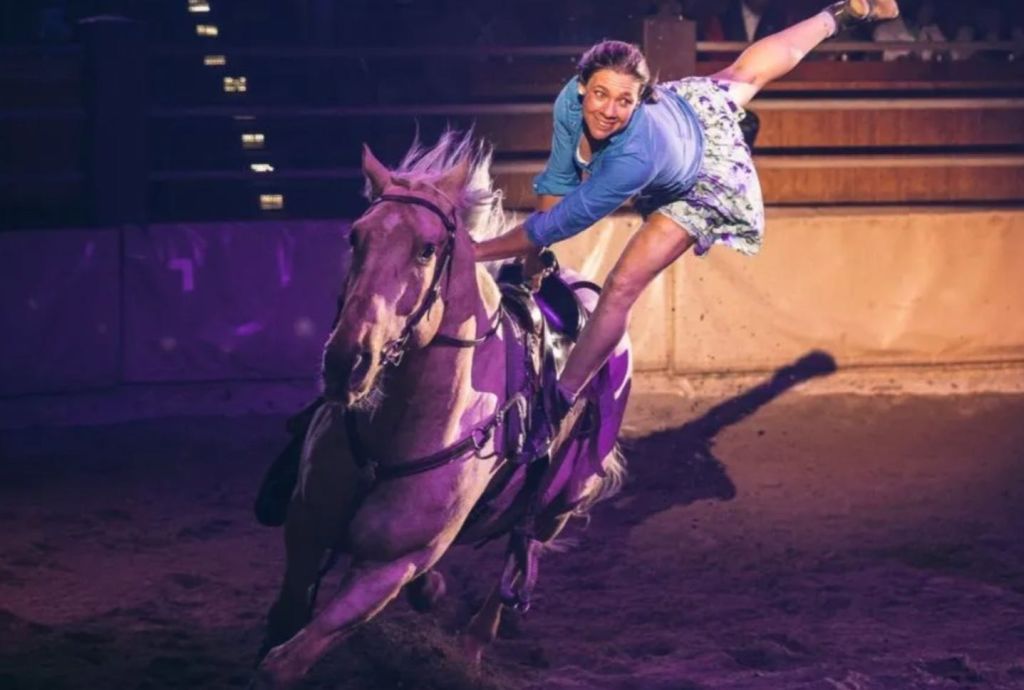 극적인 조명 아래 실내 경기장에서 질주하는 말을 타고 트릭을 하는 미드 액션의 연주자.