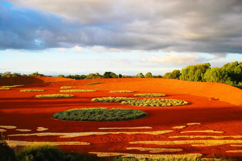 붉은 흙, 흩날리는 풀밭, 흐린 하늘이 있는 풍경. 수평선에 나무가 늘어서 있습니다.