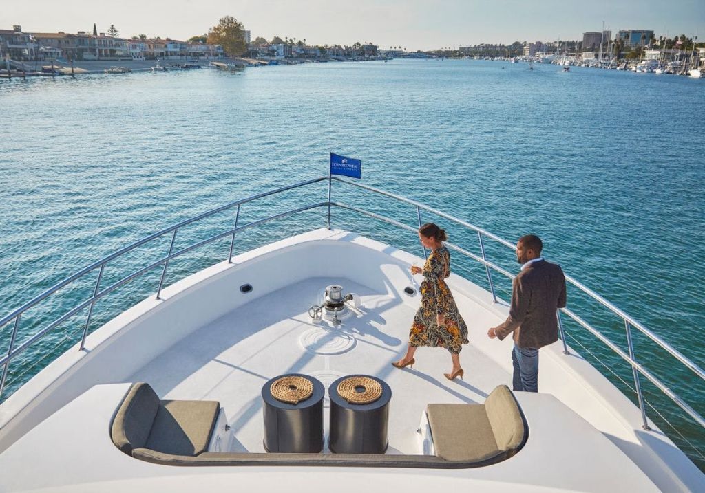 선착장과 보트를 배경으로 화창한 날 한 여성과 남성이 요트 갑판을 걷고 있습니다.