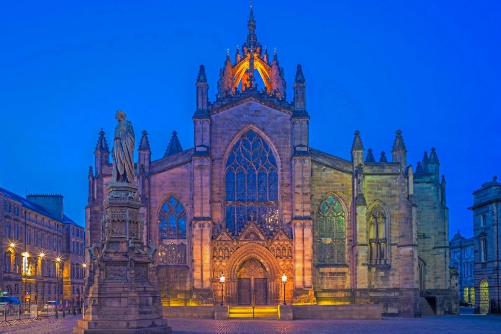 밤에는 깊고 푸른 하늘 아래 전면에 조각상이 있는 유서 깊은 교회 정면이 조명을 받습니다.