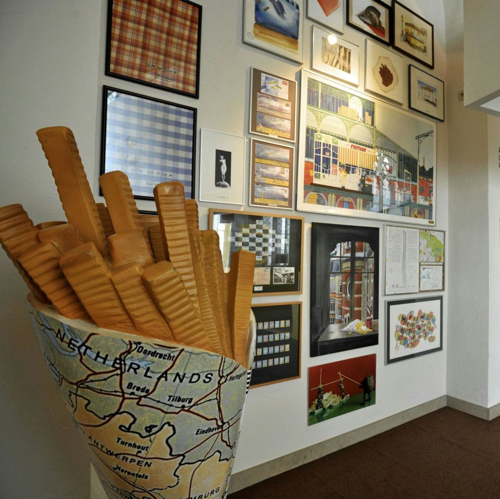 네덜란드 지도가 그려진 원뿔 모양의 크고 사실적인 프렌치 프라이 모델이 액자 예술품 벽 옆에 전시되어 있습니다.
