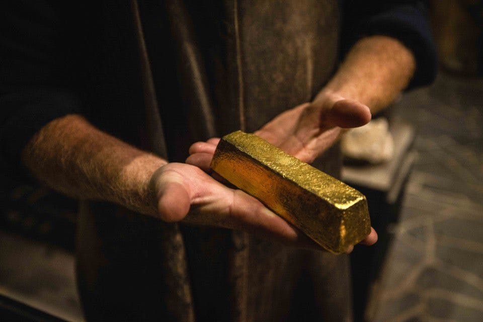 조명이 어두운 환경에서 양손으로 커다란 골드바를 들고 있는 사람.