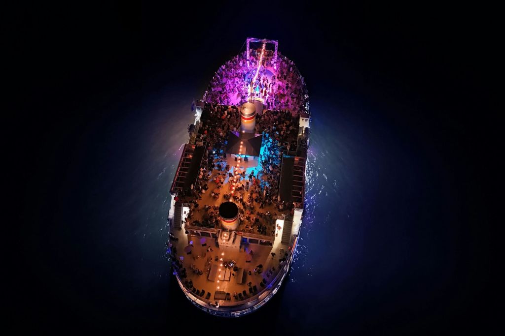 화려한 조명으로 빛나는 밤에 유람선의 공중 전망, 많은 사람들이 갑판에 모였습니다.