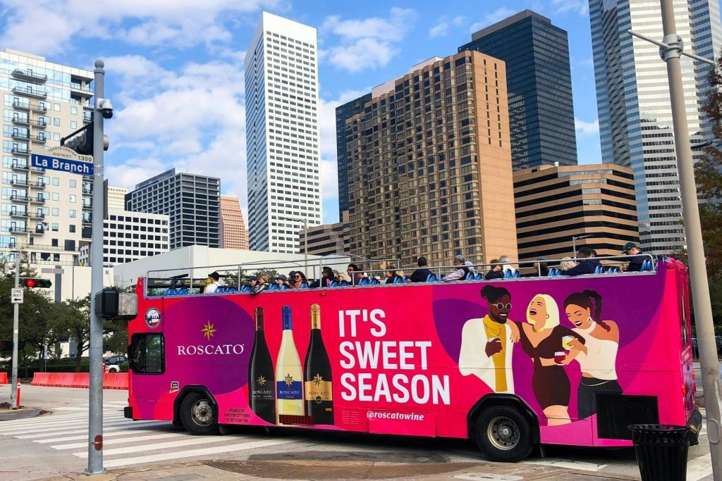 활기찬 로스카토 와인 광고가 있는 2층 버스가 부분적으로 흐린 하늘 아래 고층 빌딩을 지나갑니다.