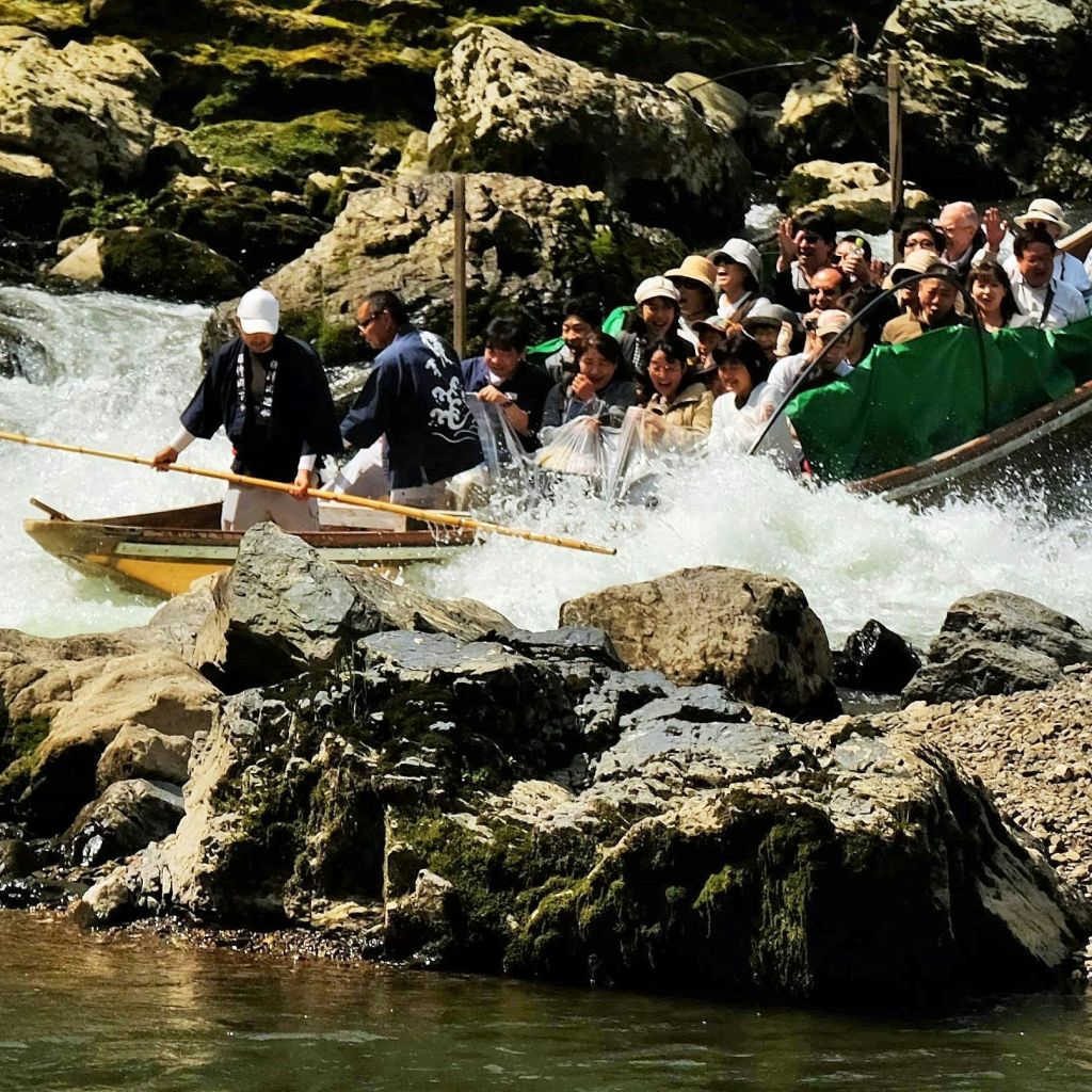 사람들이 가득한 보트가 긴 기둥을 사용하는 두 남자의 안내에 따라 강한 물살이 흐르는 바위 강을 항해합니다.