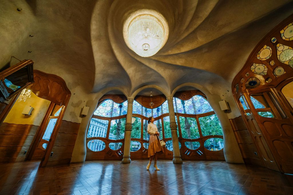 한 사람이 스테인드글라스 창문과 나선형 천장 중앙 장식이 있는 화려하게 디자인된 방에 서 있습니다.