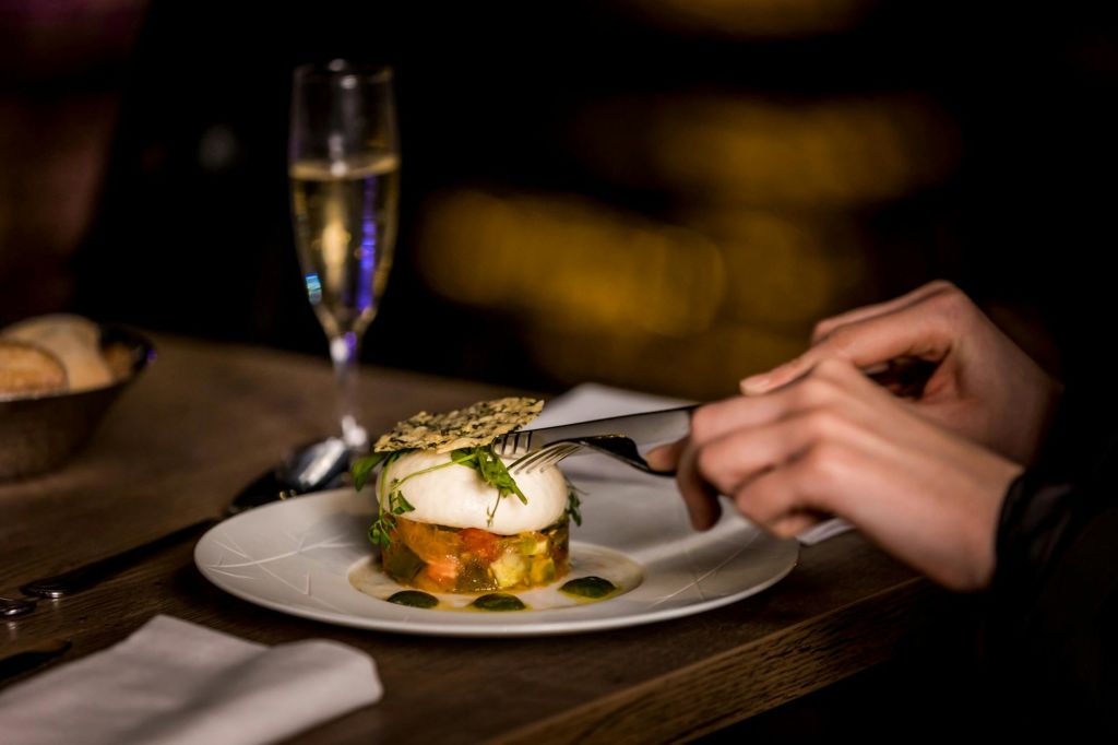 포크와 나이프를 이용해 하얀 접시에 샴페인 한 잔을 배경으로 고급 요리를 먹는 사람.